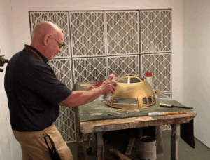 Photo of Principal Linehan putting a coat of spray paint on R2 D2 head for electronics project